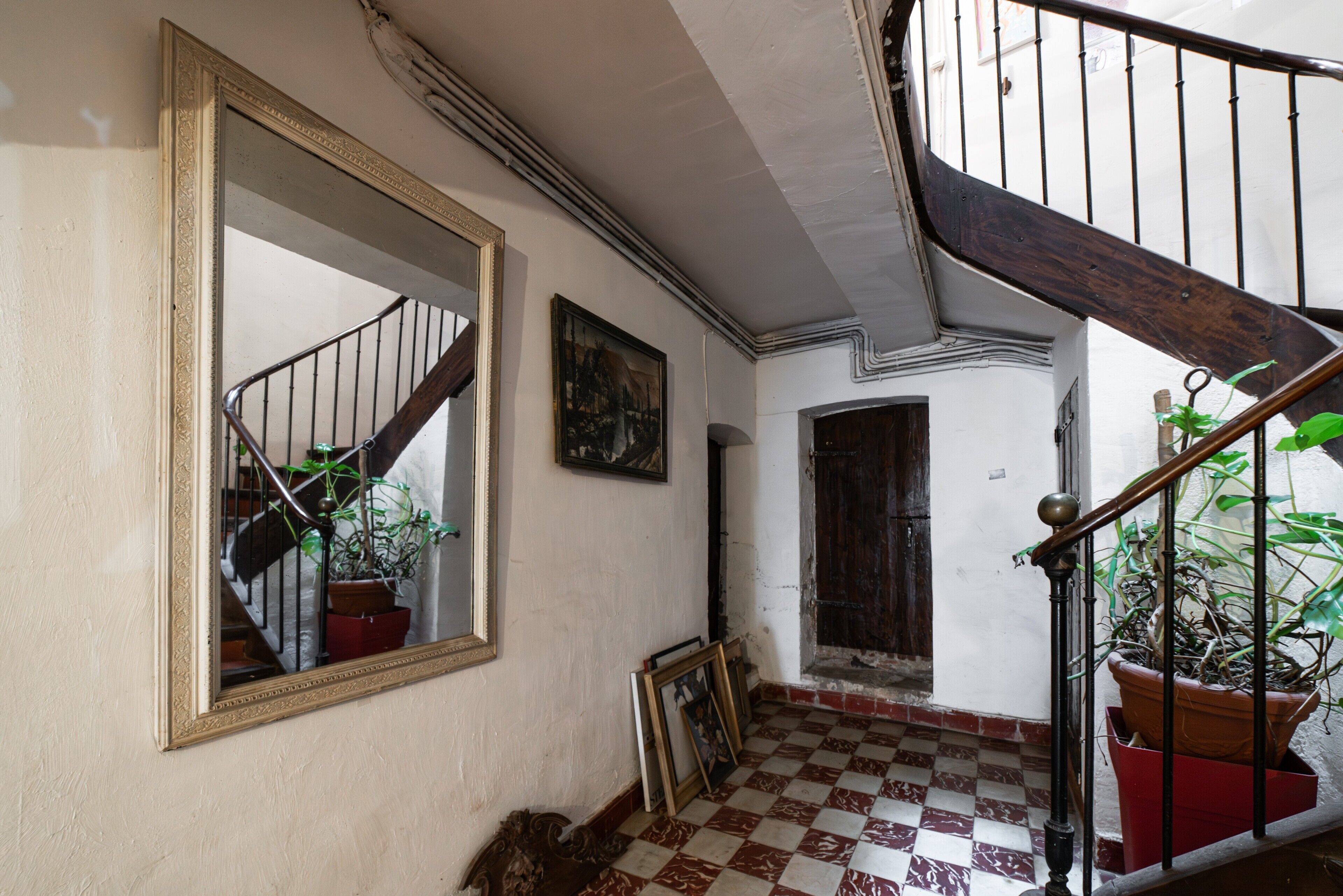 A staircase with a checkered floor, a wooden handrail, and a mirror on the wall.