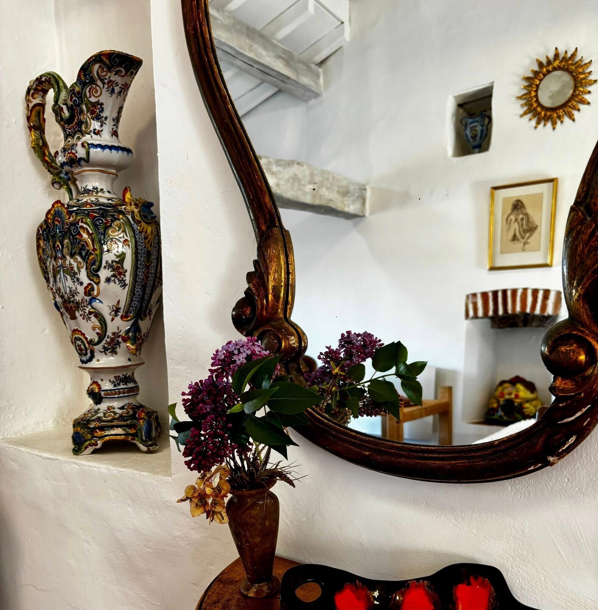 A decorative vase with a floral arrangement, a mirror, and a shelf with a figurine.