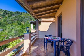 Un balcon avec une table et des chaises, un plafond en bois et une vue sur une colline.