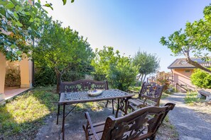 Une terrasse extérieure avec une table et des chaises, entourée de verdure et d’un mur en pierre.