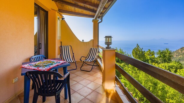 Un balcón con mesa y sillas, vista al mar y barandilla de madera.