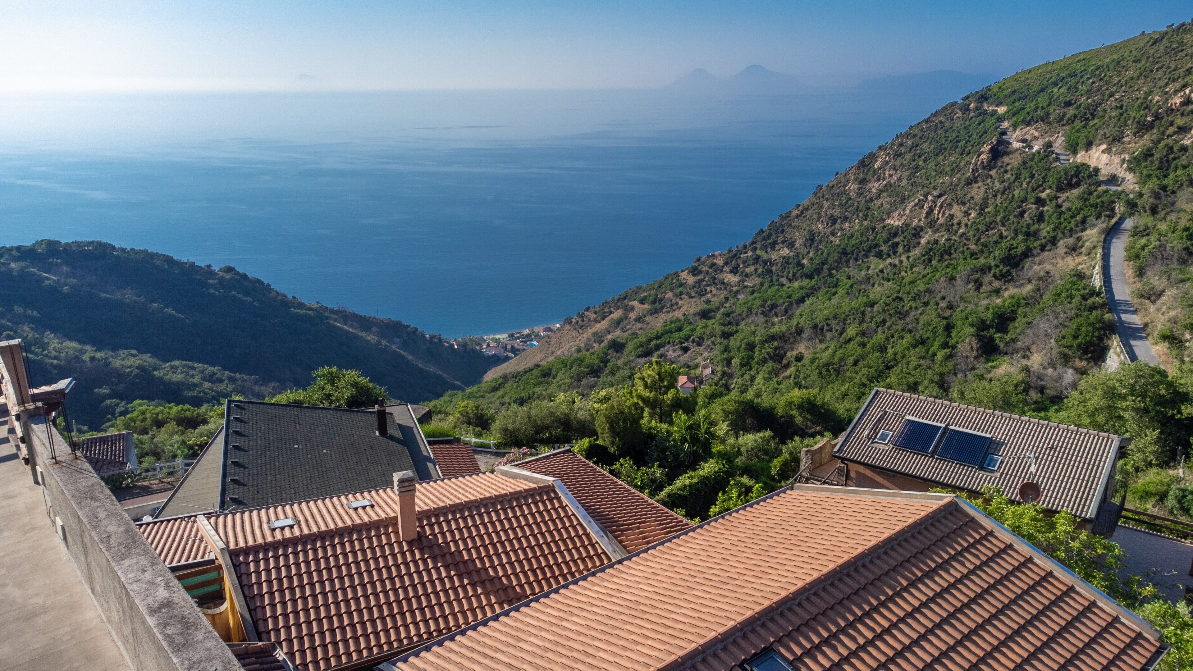 A coastal village with terracotta-roofed buildings, a winding road, and a view of the sea.