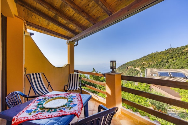 A balcony with a table, chairs, and a view of a green hillside.