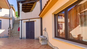 Un patio con suelo de baldosas, un banco de piedra, una escalera y una puerta.