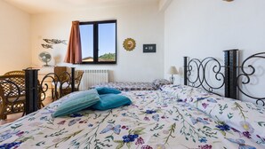 Camera da letto con un letto, due sedie, una scrivania, una finestra con tende, un termosifone e decorazioni alle pareti.