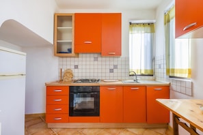 Eine Küche mit orangenen Schränken, einem Herd, einer Spüle und einem Fenster mit Vorhängen.