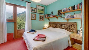 A bedroom with a bed, a nightstand, a bookshelf, and a window with curtains.
