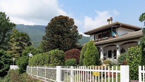 A house with a white fence, surrounded by lush greenery and a mountain backdrop.