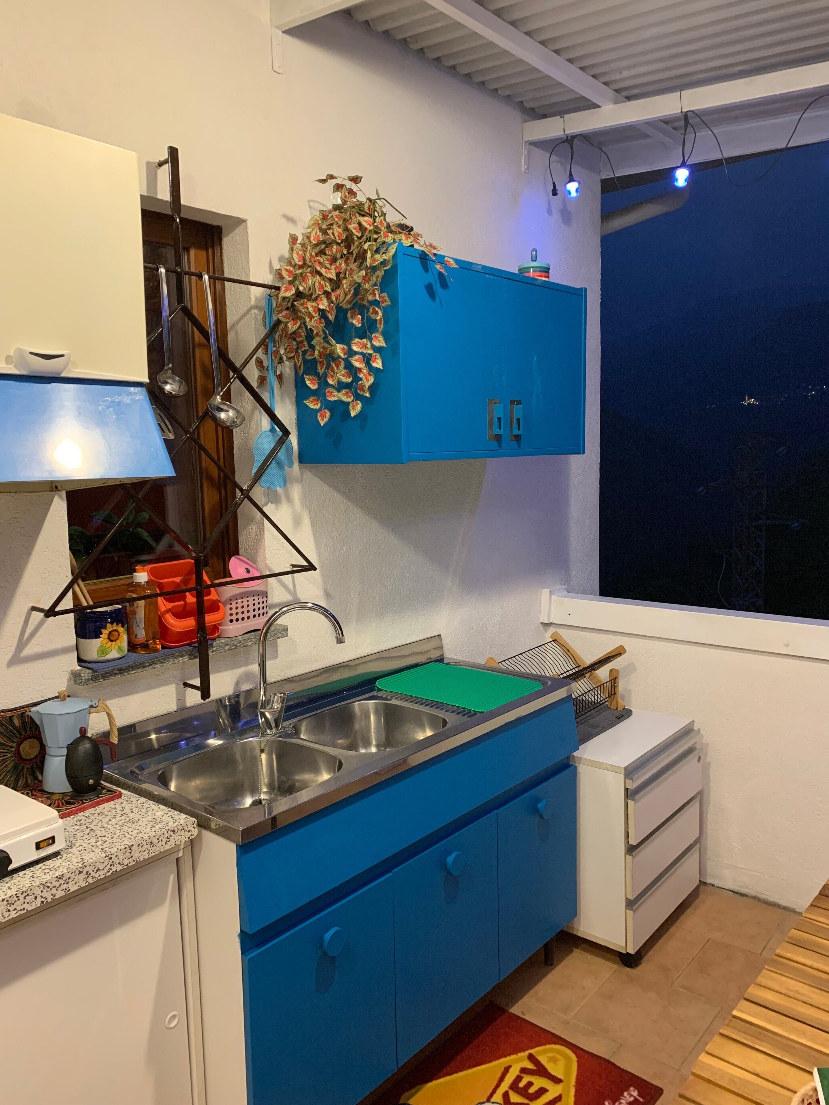 Une cuisine avec des meubles bleus, un évier en acier inoxydable et une fenêtre donnant sur la ville, avec une vue particulièrement belle la nuit.