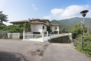 A white house with a balcony, a gated driveway, and a mountain backdrop.