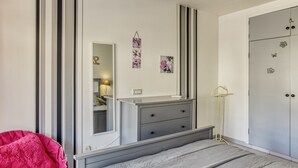 Een slaapkamer met een bed, een dressoir, een spiegel en een kledingkast.