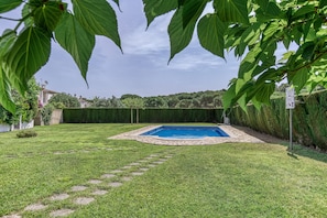 A backyard with a swimming pool, surrounded by well-maintained grass and a stone border.