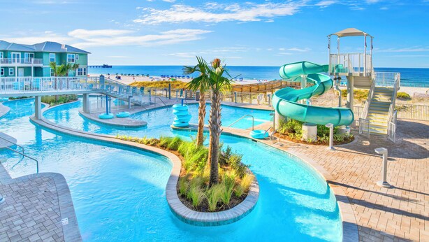 Une piscine avec un toboggan, des palmiers et une vue sur la plage.