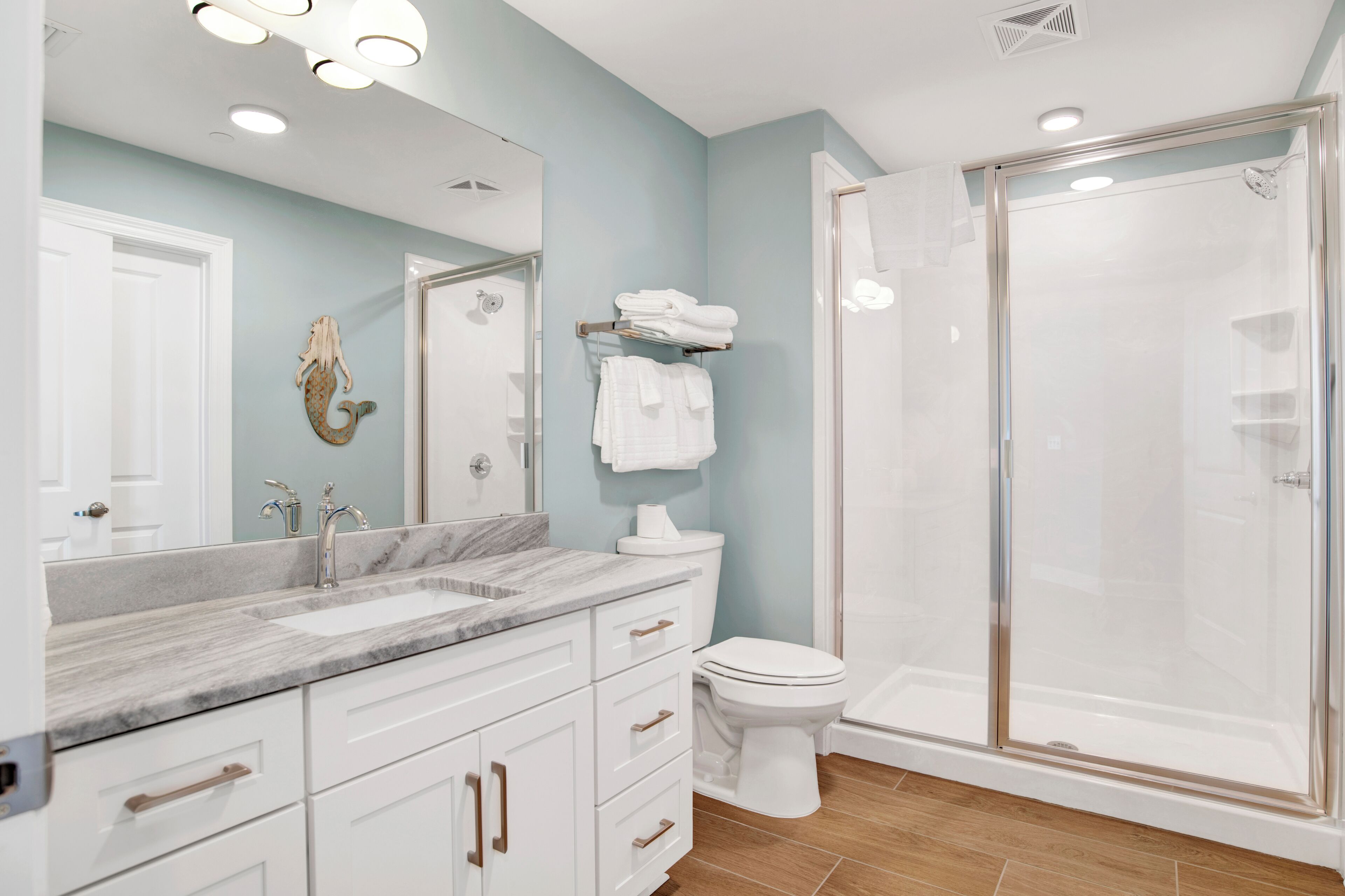A bathroom with a marble sink, white cabinets, a toilet, and a glass-enclosed shower.