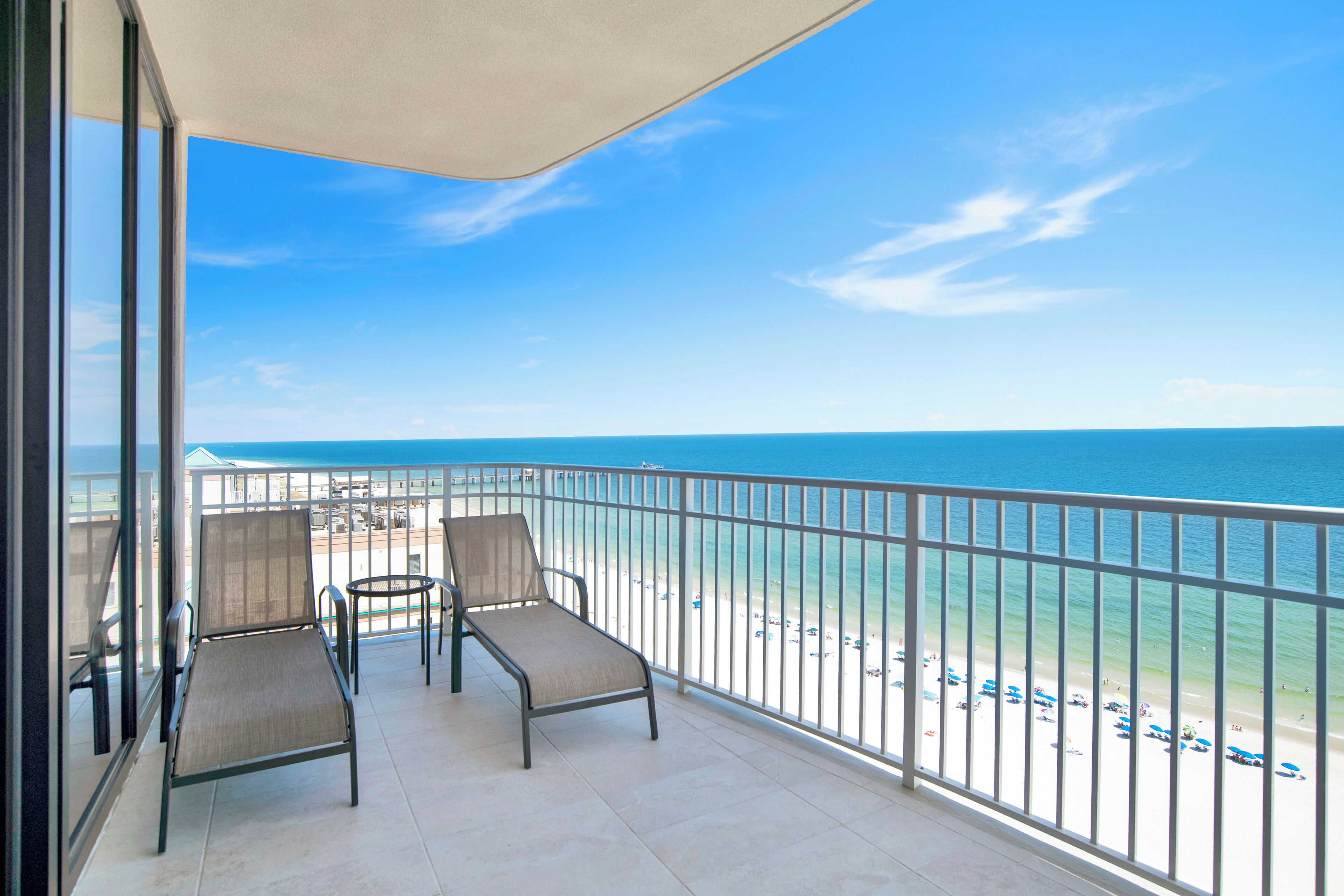 A balcony with two chairs and a table, overlooking a beach with a clear view of the ocean.