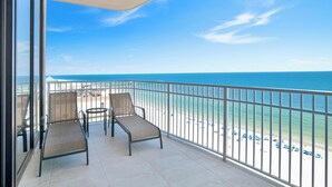 Un balcon avec deux chaises et une table, donnant sur une plage et offrant une vue dégagée sur l’océan.