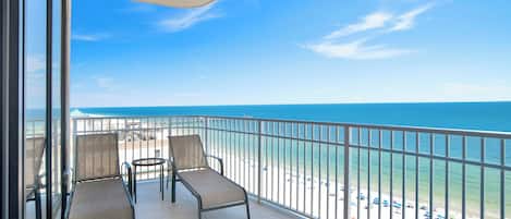 A balcony with two chairs and a table, overlooking a beach with a clear view of the ocean.