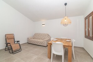 Un coin repas avec une table en bois, des chaises blanches, un canapé à motifs et un luminaire suspendu.