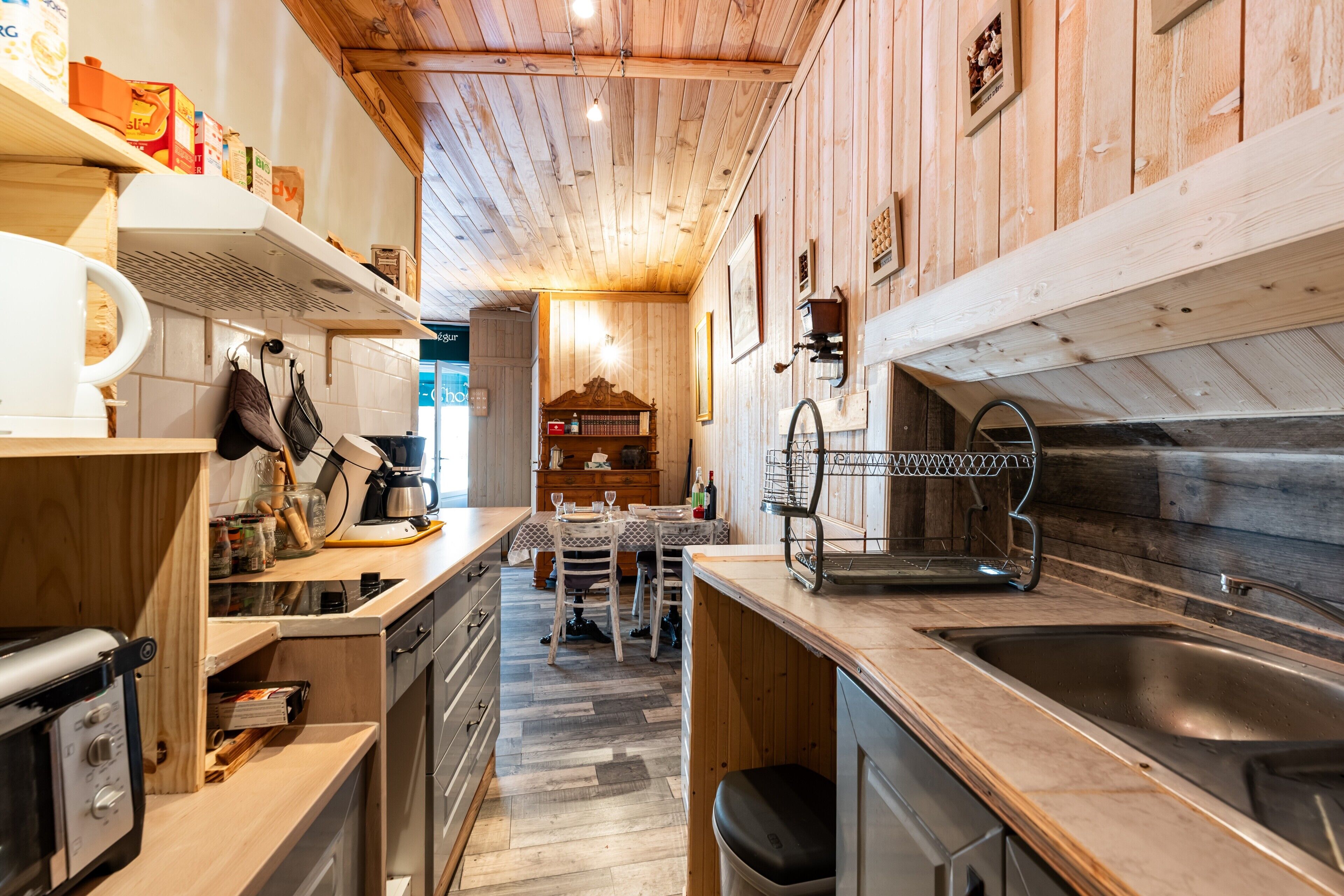 Une cuisine avec des meubles en bois, un évier en acier inoxydable et un coin repas comprenant une table et des chaises.