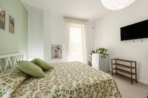 A bedroom with a bed, a TV mounted on the wall, a plant, and a shelf unit. - Guest House 'Lovi Room' with Private Terrace, Wi-Fi and Air Conditioning (Capaci)
