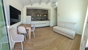 A modern kitchen with a built-in oven, a dining area with a wooden table and chairs, and a beige sofa in a living room. - Apartment in semi-detached villa nestled in the Ragusa countryside (Ragusa)
