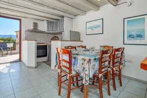 A dining area with a table set for four, surrounded by wooden chairs, a kitchen in the background, and a view of the outdoors. - Apartment 'Flamingo' with Private Terrace, Balcony and Air Conditioning (san teodoro)