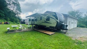 A recreational vehicle with a ramp leading to a house, a picnic table, and outdoor chairs. - Cozy RV in charming McClure with AC, WiFi. Happy travels (McClure)