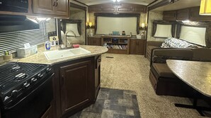 A compact RV kitchen with a stove, microwave, sink, and a dining area with a table and couch.