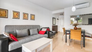 Ein modernes Wohnzimmer mit einem grauen Sofa, einem weißen Couchtisch, einem Esstisch mit Stühlen und gerahmten Kunstwerken an der Wand.