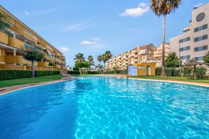 A swimming pool surrounded by multi-story buildings with balconies, palm trees, and a clear sky. - Apartment 'Las Brisas' with Mountain View, Wi-Fi and Air Conditioning (Dénia)