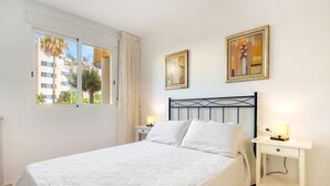 Ein Schlafzimmer mit einem Bett, zwei Nachttischen, einem Fenster mit Vorhängen und zwei gerahmten Kunstwerken an der Wand.