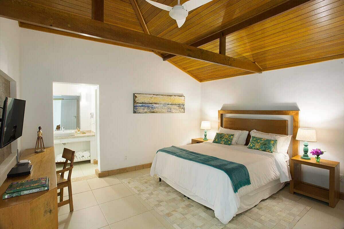 Ein Schlafzimmer mit Holzboden, einem Bett mit weißer Bettwäsche, einem Schreibtisch mit Stuhl, einem Fernseher und einem Gemälde an der Wand.