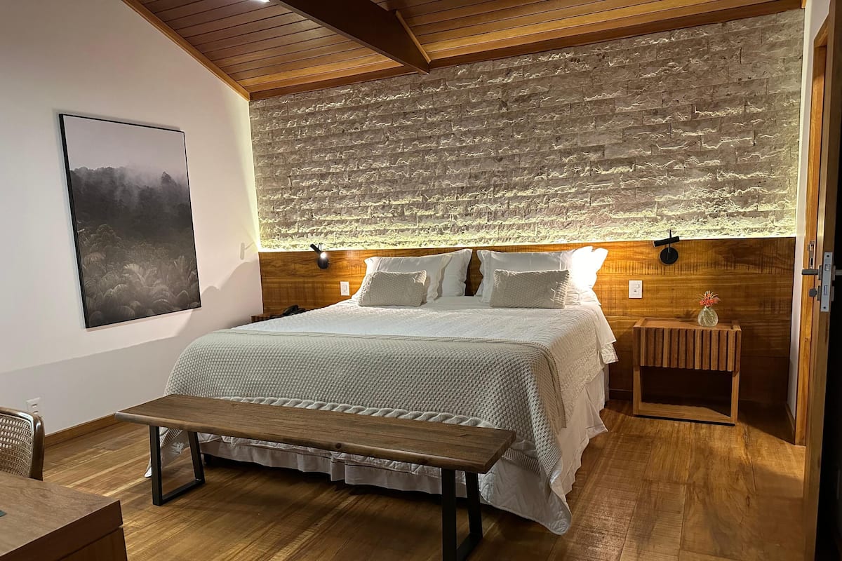 Ein Schlafzimmer mit einem großen Bett, einer hölzernen Bank, einem Nachttisch und einer Wandleuchte.