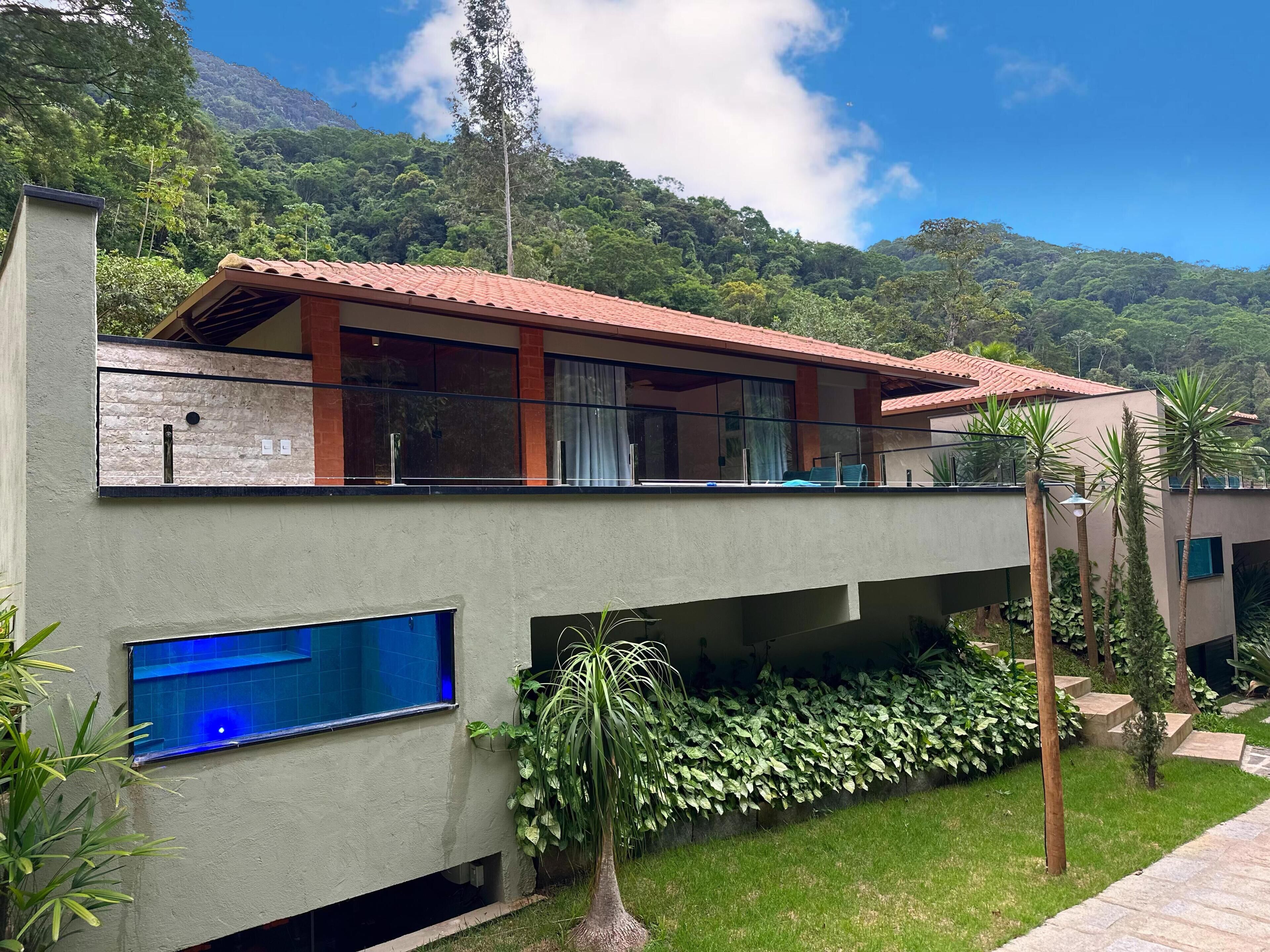 A modern two-story building with a balcony, large windows, and a view of a lush mountain.