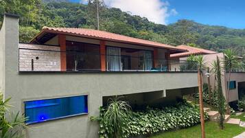 A modern two-story building with a balcony, large windows, and a view of a lush mountain.