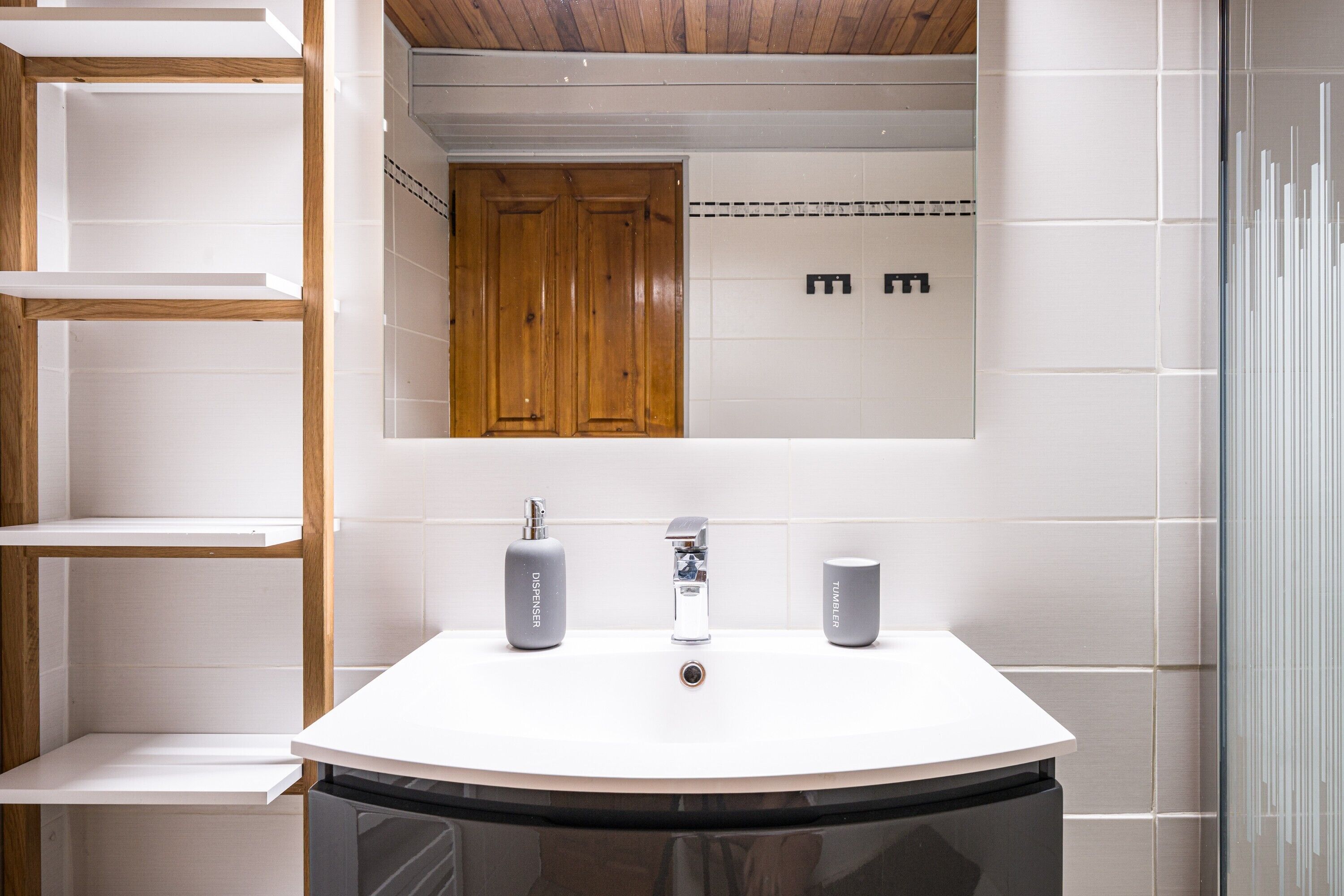 Un baño con un lavabo blanco, dos dispensadores grises, un espejo y armarios de madera.