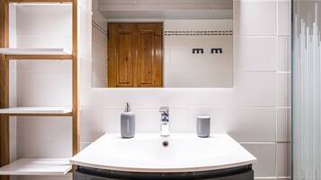 Un baño con un lavabo blanco, dos dispensadores grises, un espejo y armarios de madera.
