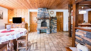 A rustic interior with a stone fireplace, wooden ceiling, and a dining area with a table and chairs.