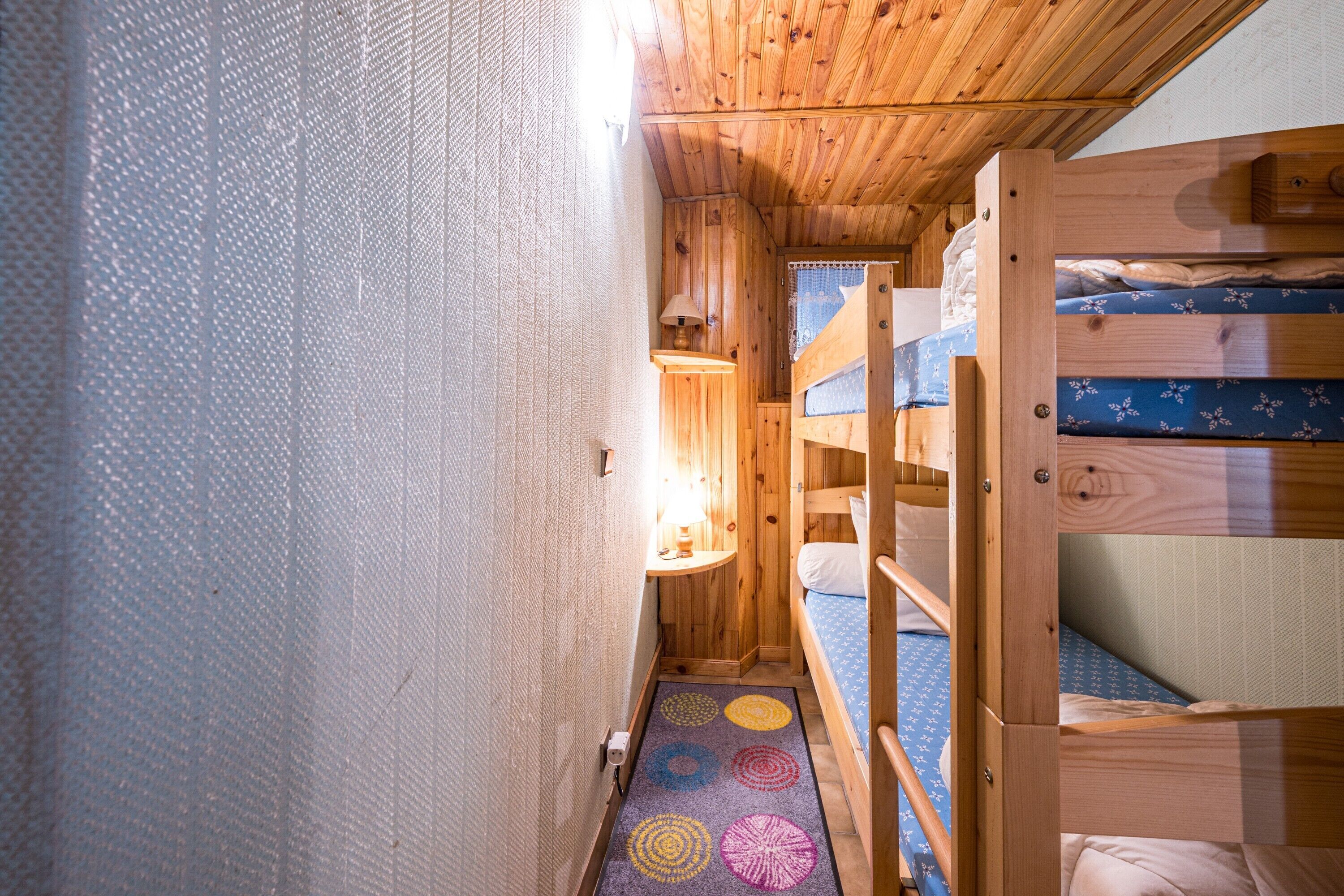 Um corredor estreito com beliches de madeira, uma luminária e um tapete estampado.