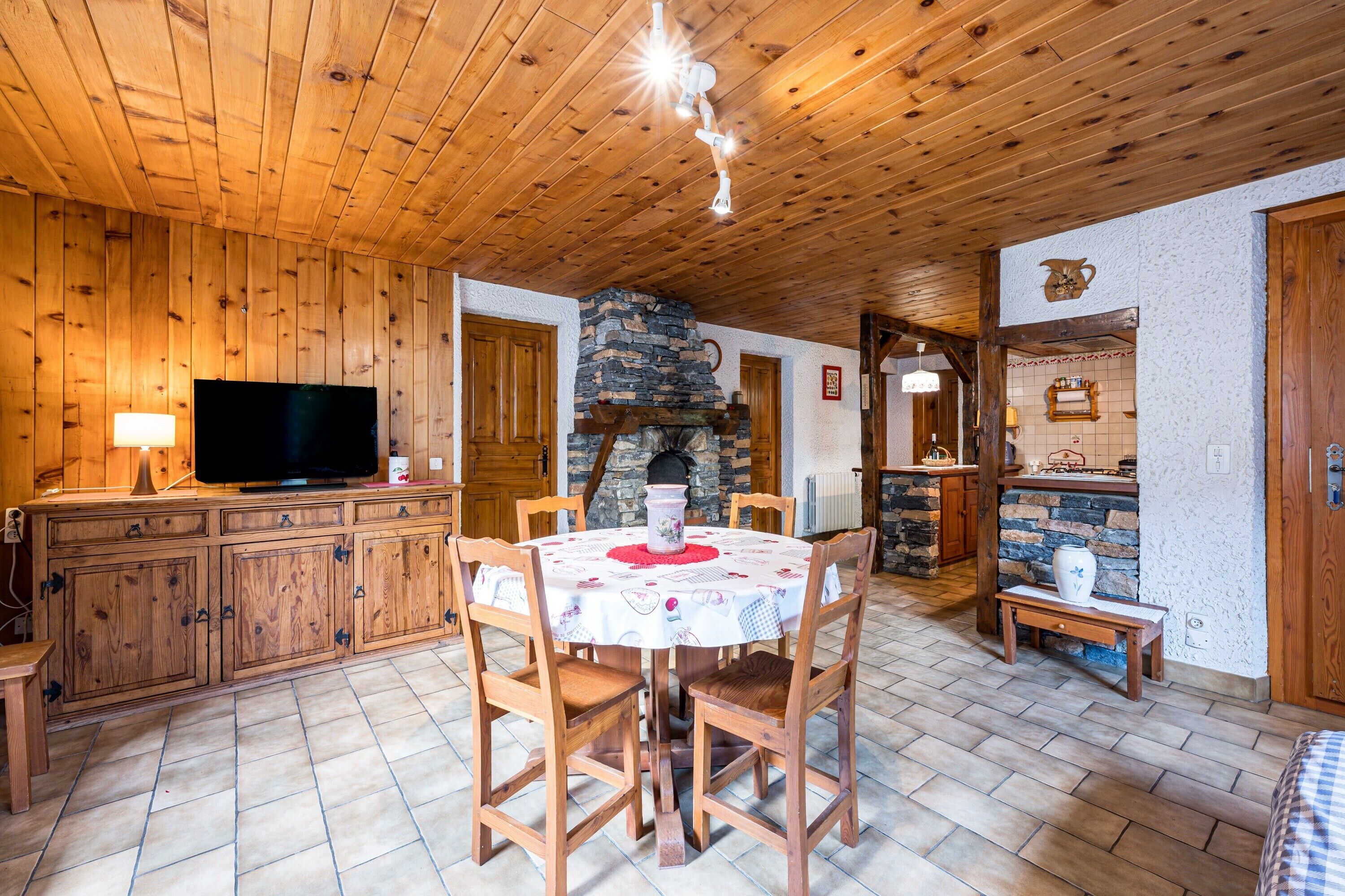 Una stanza con rivestimento in legno, un camino in pietra, una televisione e un tavolo da pranzo con sedie.
