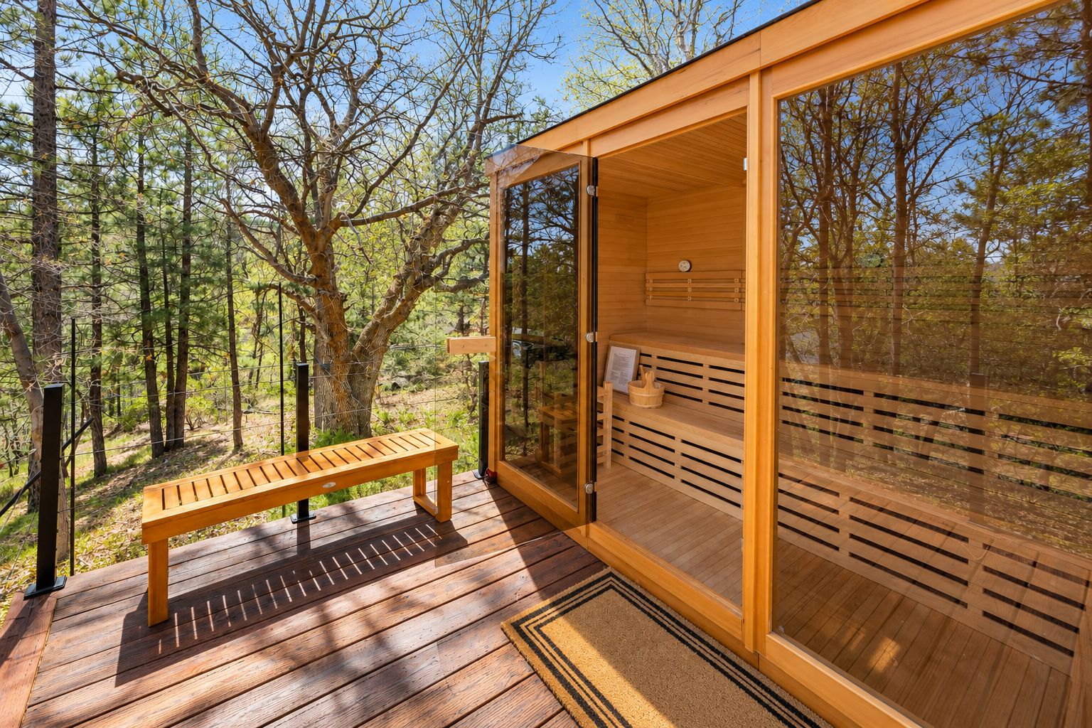 Een houten sauna met een bank en een glazen deur, gelegen in een bebost gebied.
