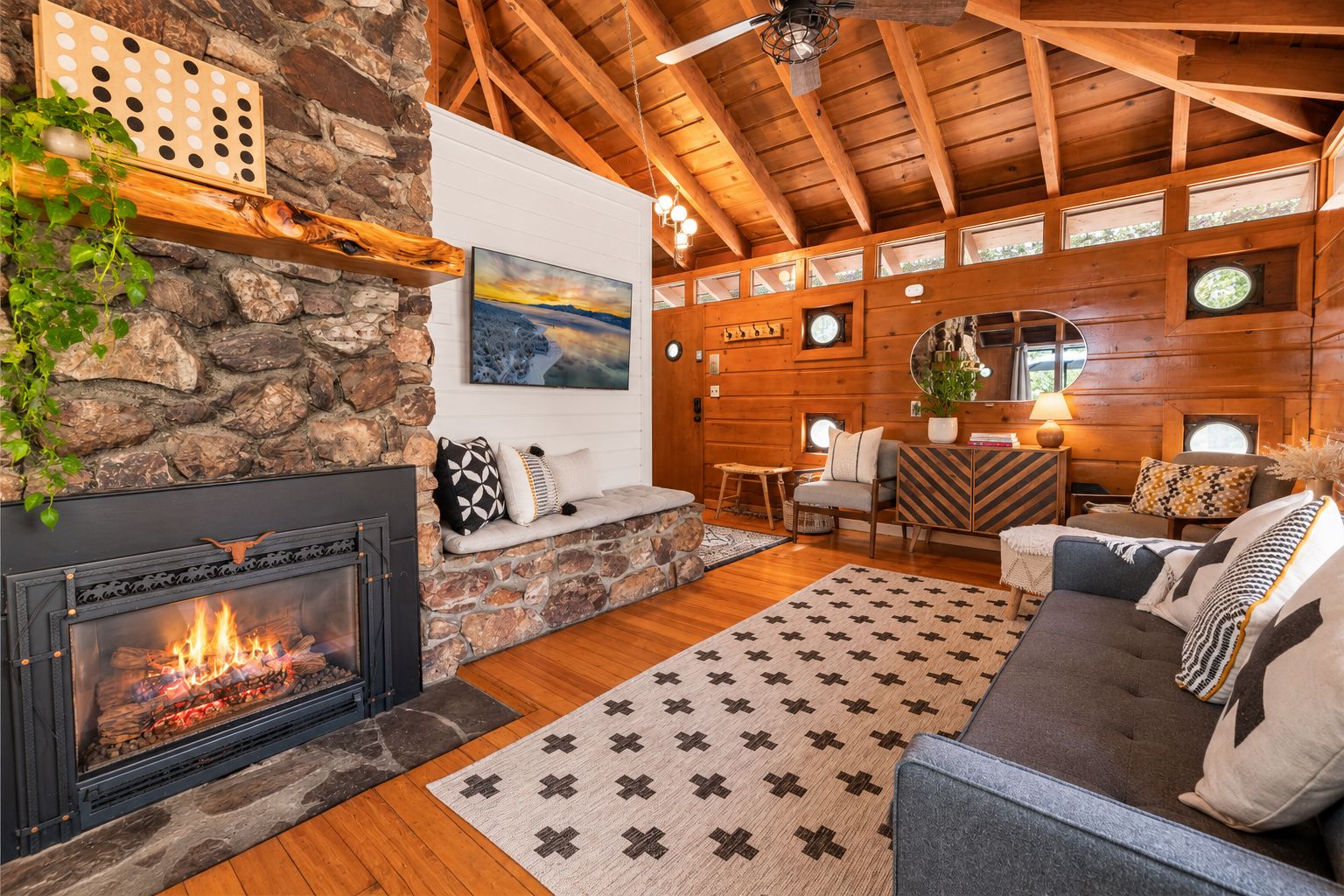 Interior acogedor de una cabaña con chimenea de piedra, vigas de techo de madera, una zona de estar confortable y un ventanal grande.