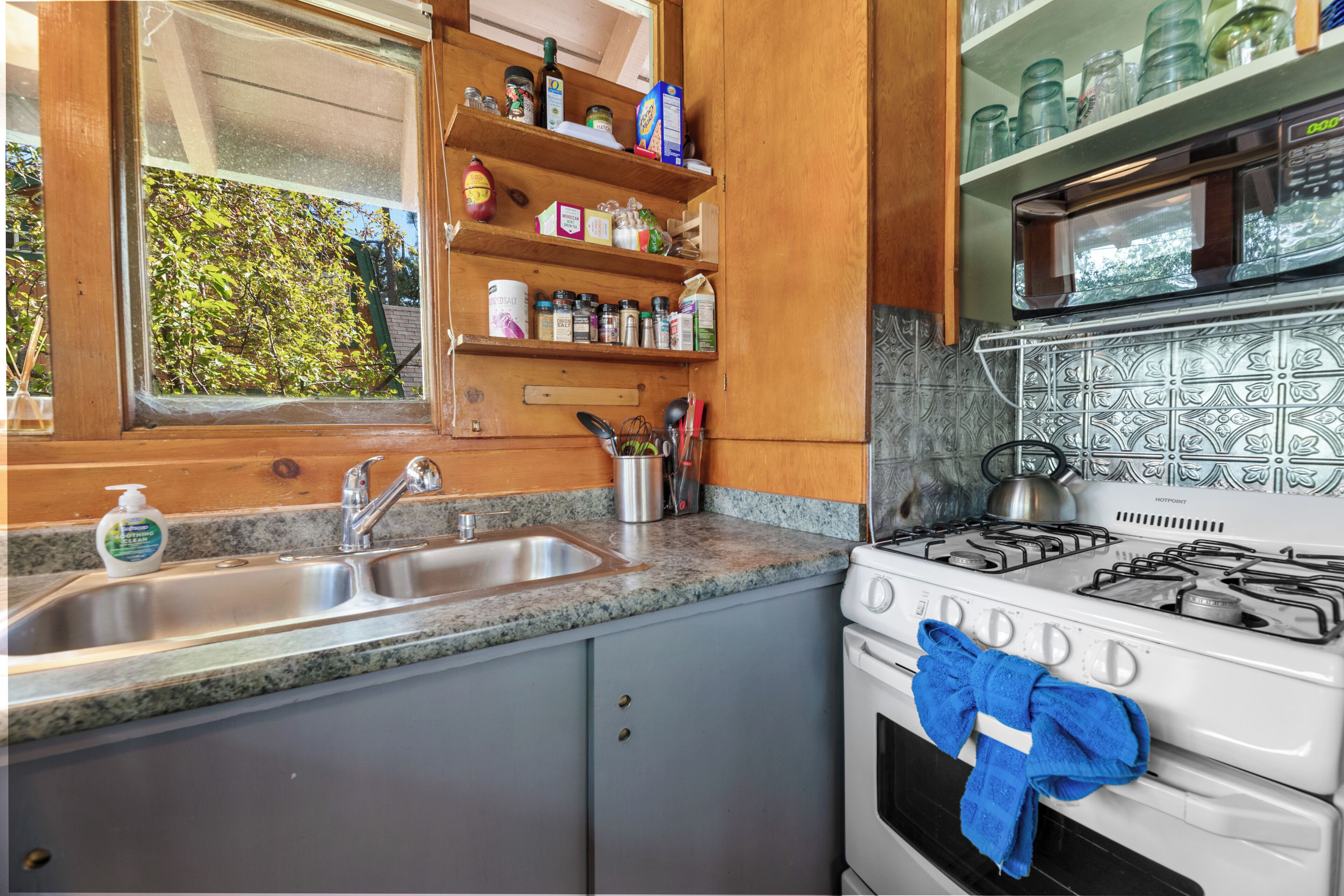 Une cuisine dotée d’un plan de travail en granit, d’un évier en acier inoxydable, de meubles en bois et d’une cuisinière blanche sur laquelle est accrochée une serviette bleue.