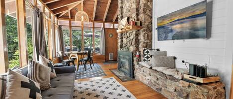 A cozy living room with a stone wall, wooden ceiling, and a fireplace. There is a sofa, a rug, and a painting on the wall.