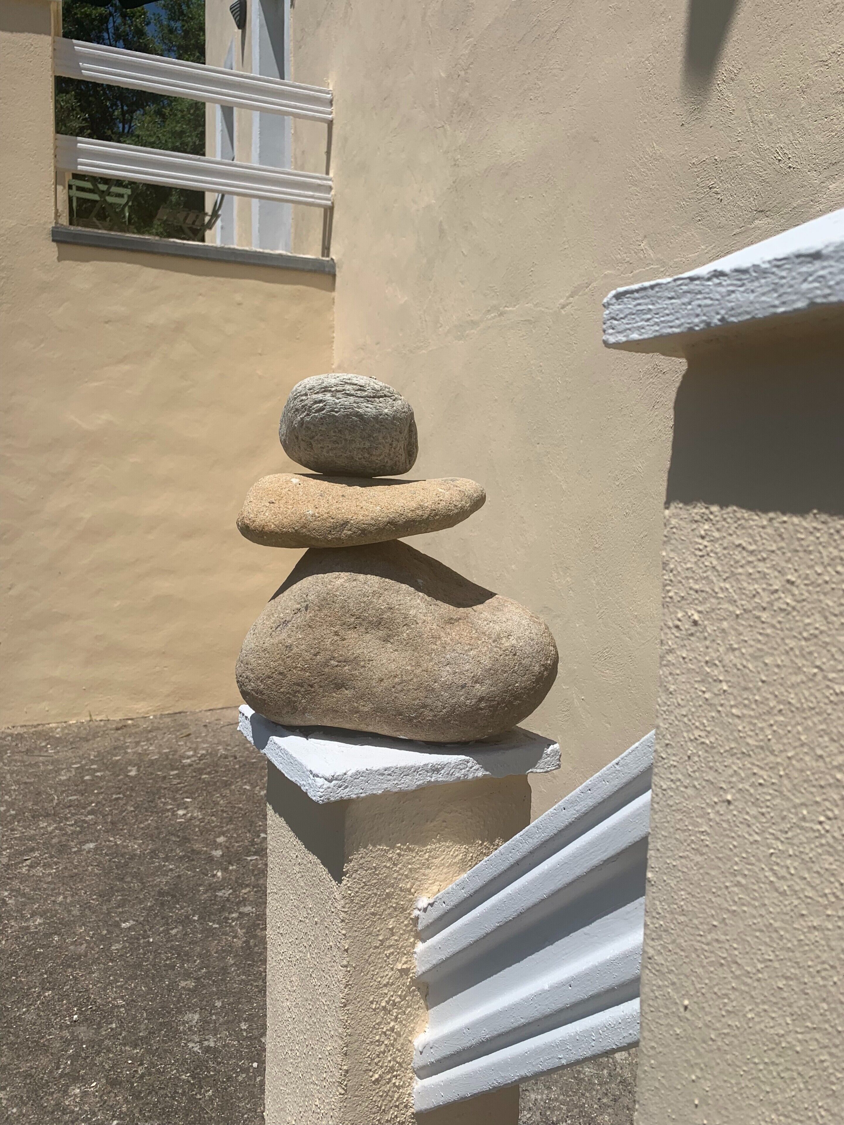 Un équilibre de pierres posé sur une corniche blanche, adossé à un mur beige.