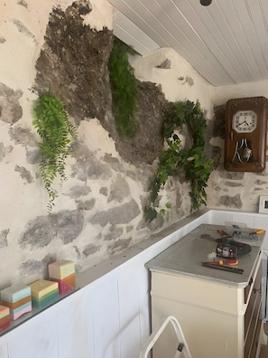 A kitchen with a stone wall, a wooden clock, and a countertop with tools and a microwave.