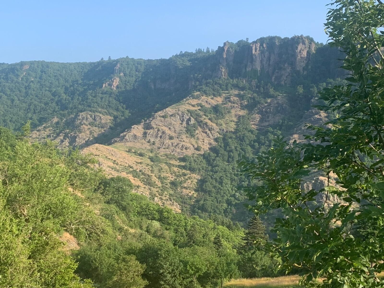 A mountainous landscape with dense forest and rocky cliffs.