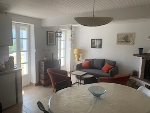A dining area with a round table, chairs, a glass bowl centerpiece, a sofa with cushions, a lamp, and a fireplace.