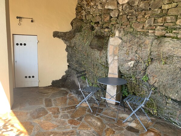 A stone patio with a white door, a small round table, and two metal chairs.