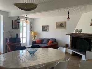 A living room with a round table, a sofa, a fireplace, and a ceiling with exposed beams.